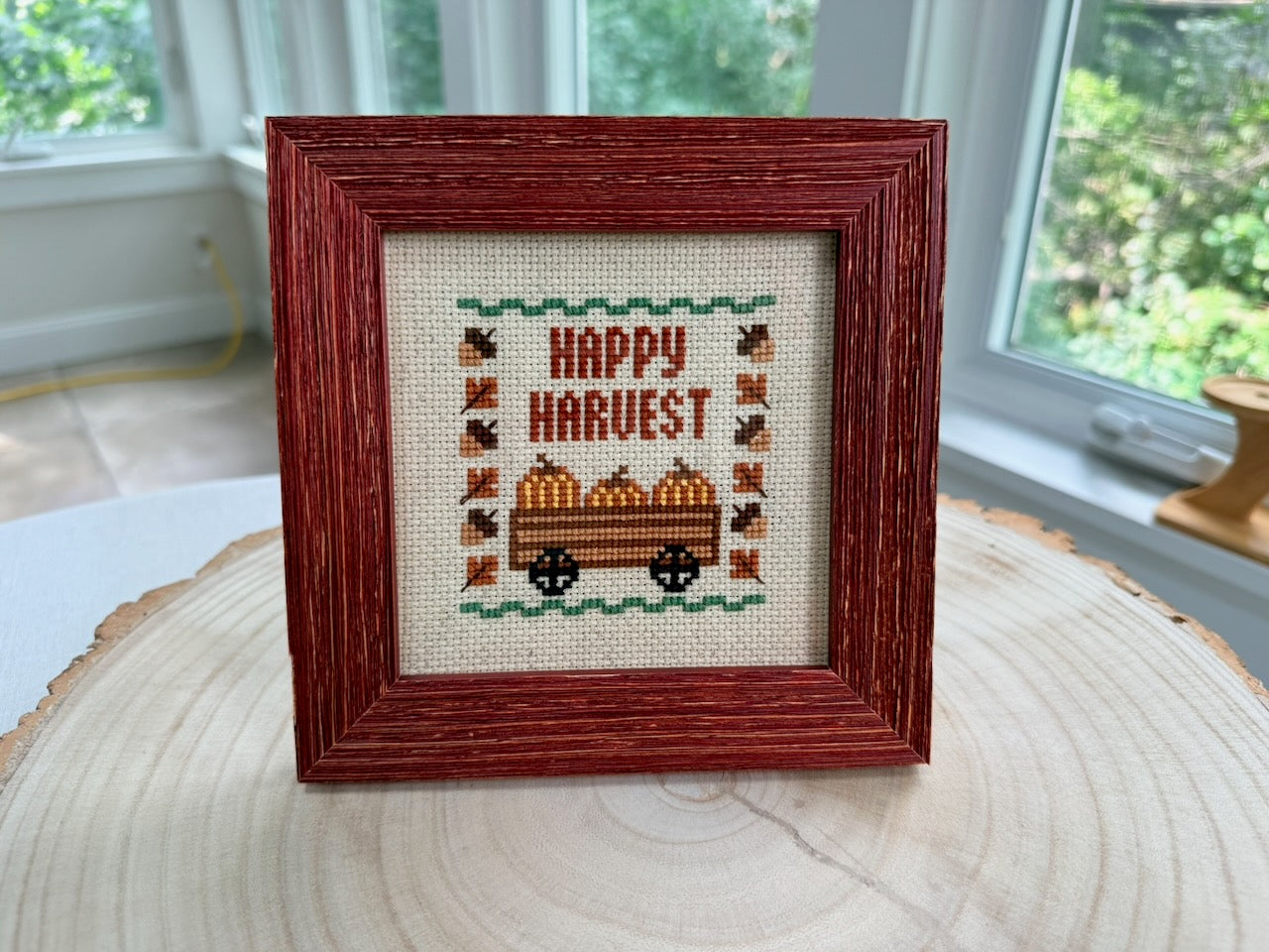 Framed Fall Happy Harvest cross stitch with pumpkin wagon, acorns and leaves, burgundy frame