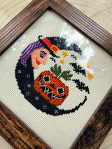 Halloween Witch Moon cross stitch close-up showing witch, jack-o'-lantern, and bats in a brown frame
