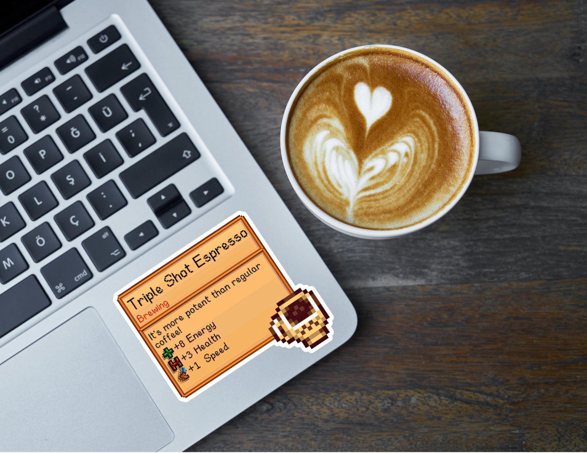 Stardew Valley Triple Shot Espresso die-cut sticker on a laptop next to a latte with heart latte art