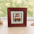Fall Happy Harvest cross stitch framed, styled cover shot with pumpkin and leaf on wood table