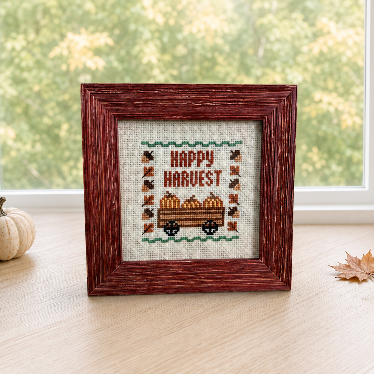 Fall Happy Harvest cross stitch framed, styled cover shot with pumpkin and leaf on wood table