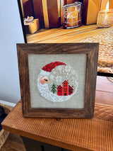 Framed cross-stitch, Santa Christmas Village, brown frame detail view